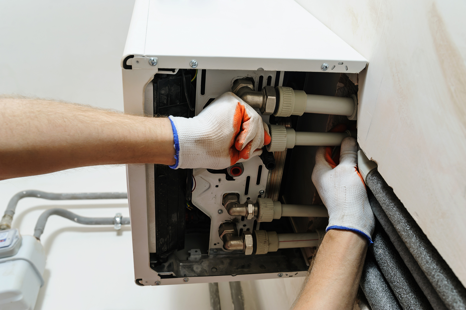 Installation of home heating. A worker attaches the pipe to the gas boiler.